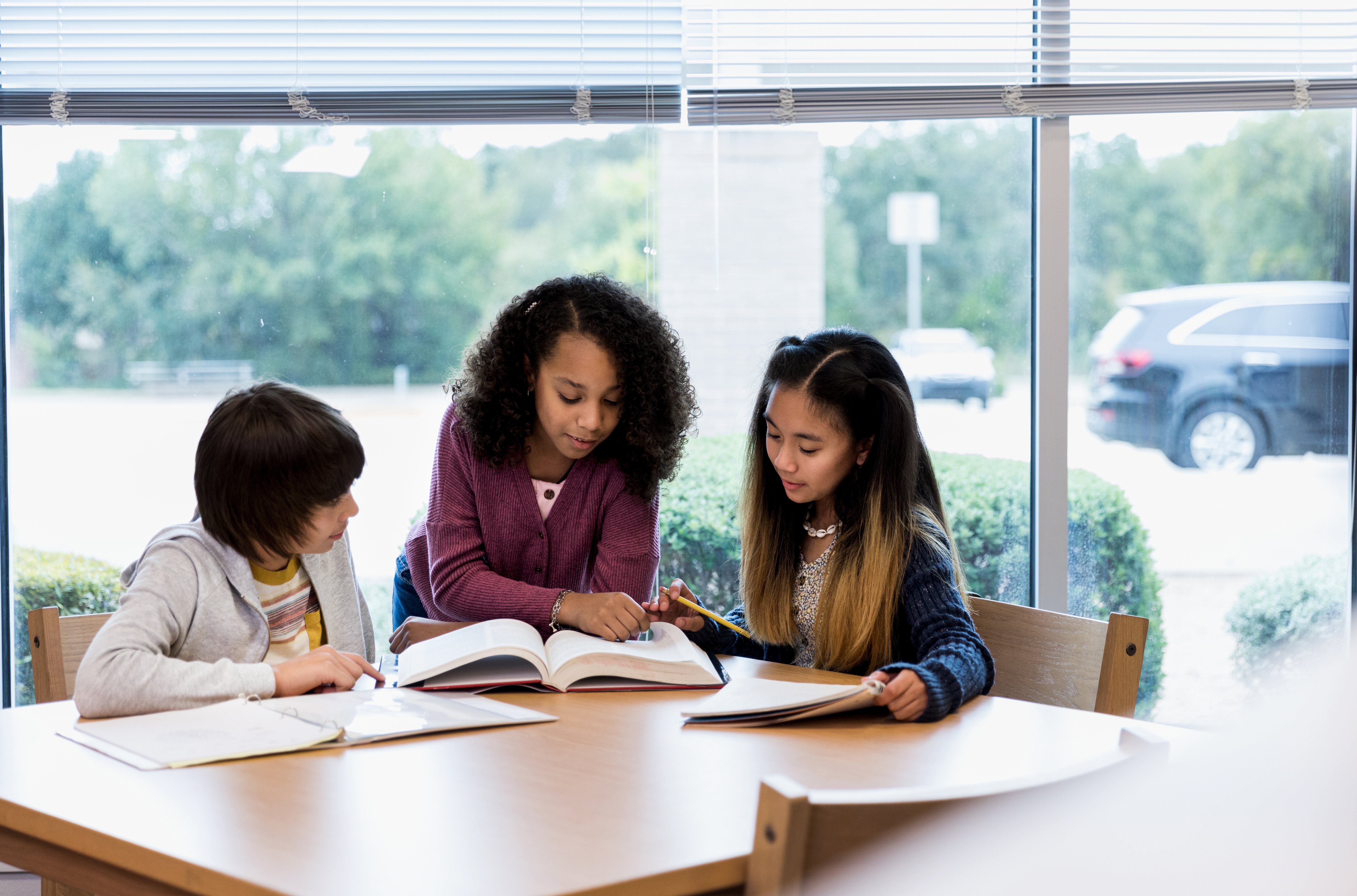 3 middle school aged students sitting at a table with a book working on their reading skills 